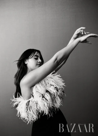 Black and white portrait of an adult female in elegant black dress with feather boa, set against a neutral gray background.