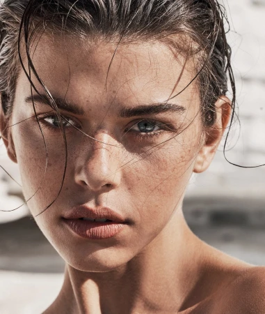 Close-up portrait of a woman with wet dark hair and natural skin texture with freckles by make-up artist Victoria Baron