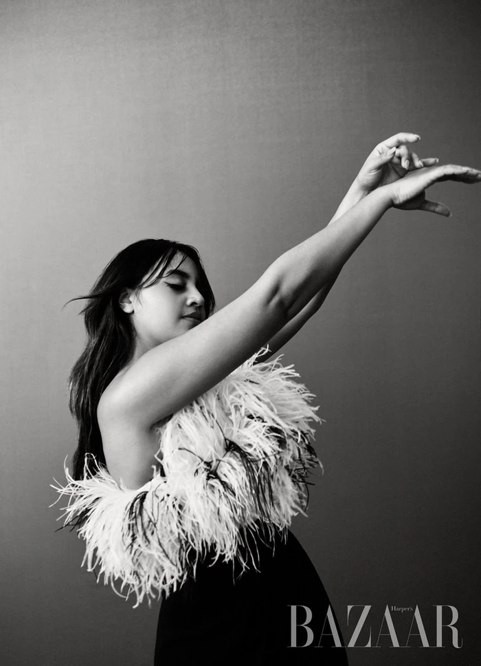 Black and white portrait of a woman in a feather top with arms raised, makeup by Victoria Baron.