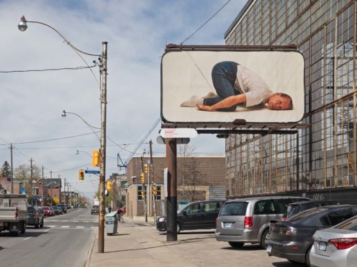 Billboard displays a photograph of a woman in yoga pose, seen from street level with parked cars and buildings in the background.
