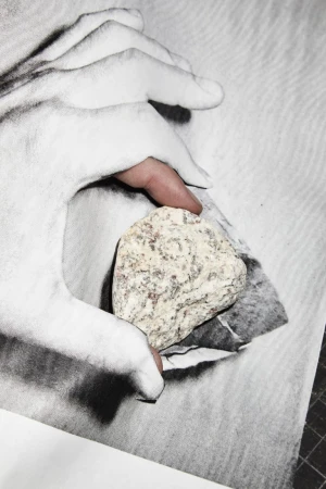 Close-up of a hand painted white holding a textured speckled stone against a monochrome patterned background.