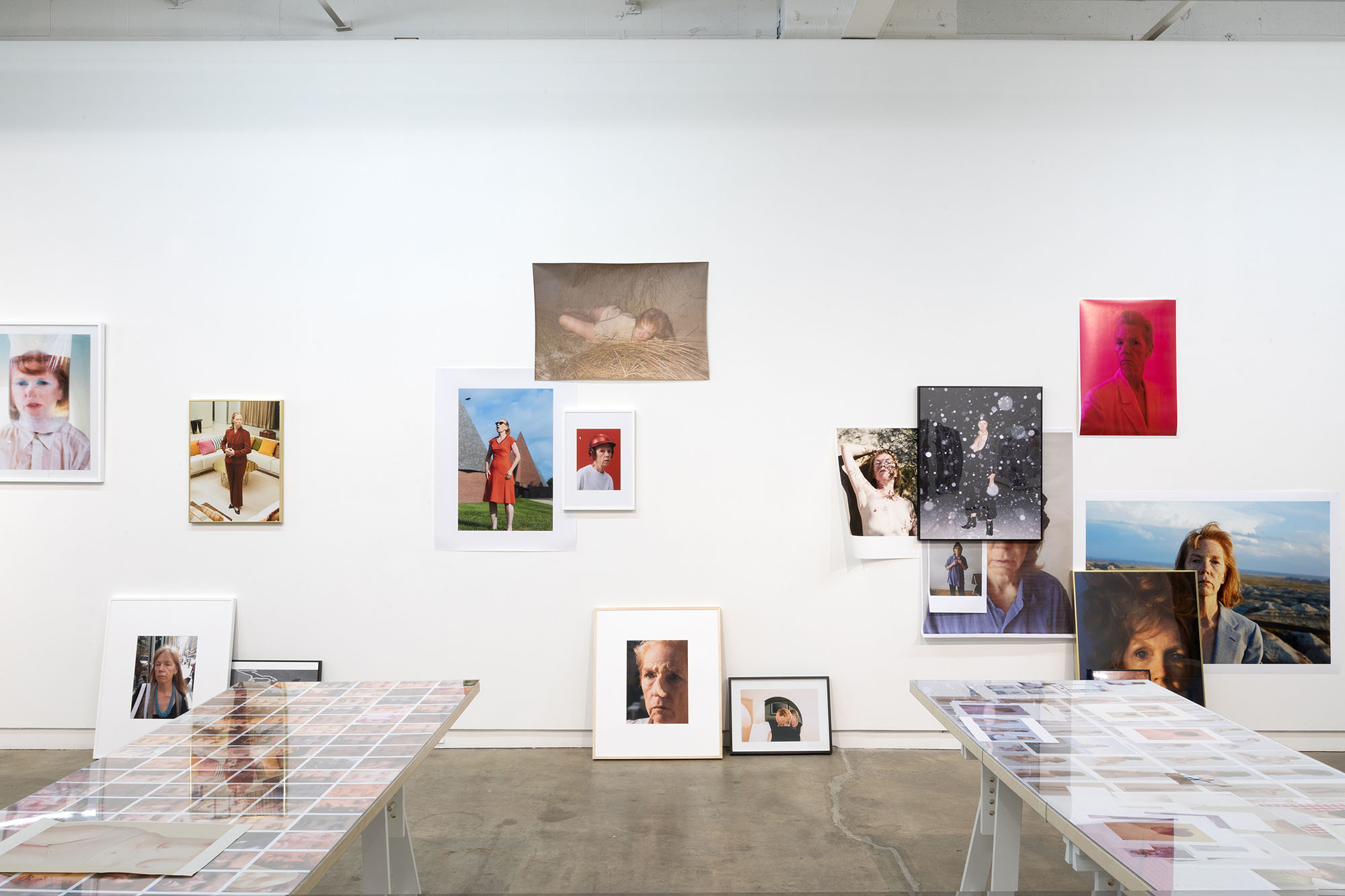 Photo exhibit showcasing various framed portraits of people hanging on a white wall, with tables displaying additional photos in the foreground.