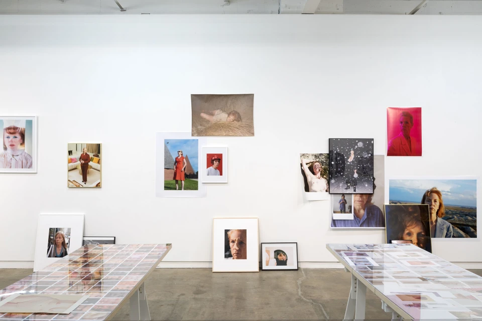 Photo exhibit showcasing various framed portraits of people hanging on a white wall, with tables displaying additional photos in the foreground.
