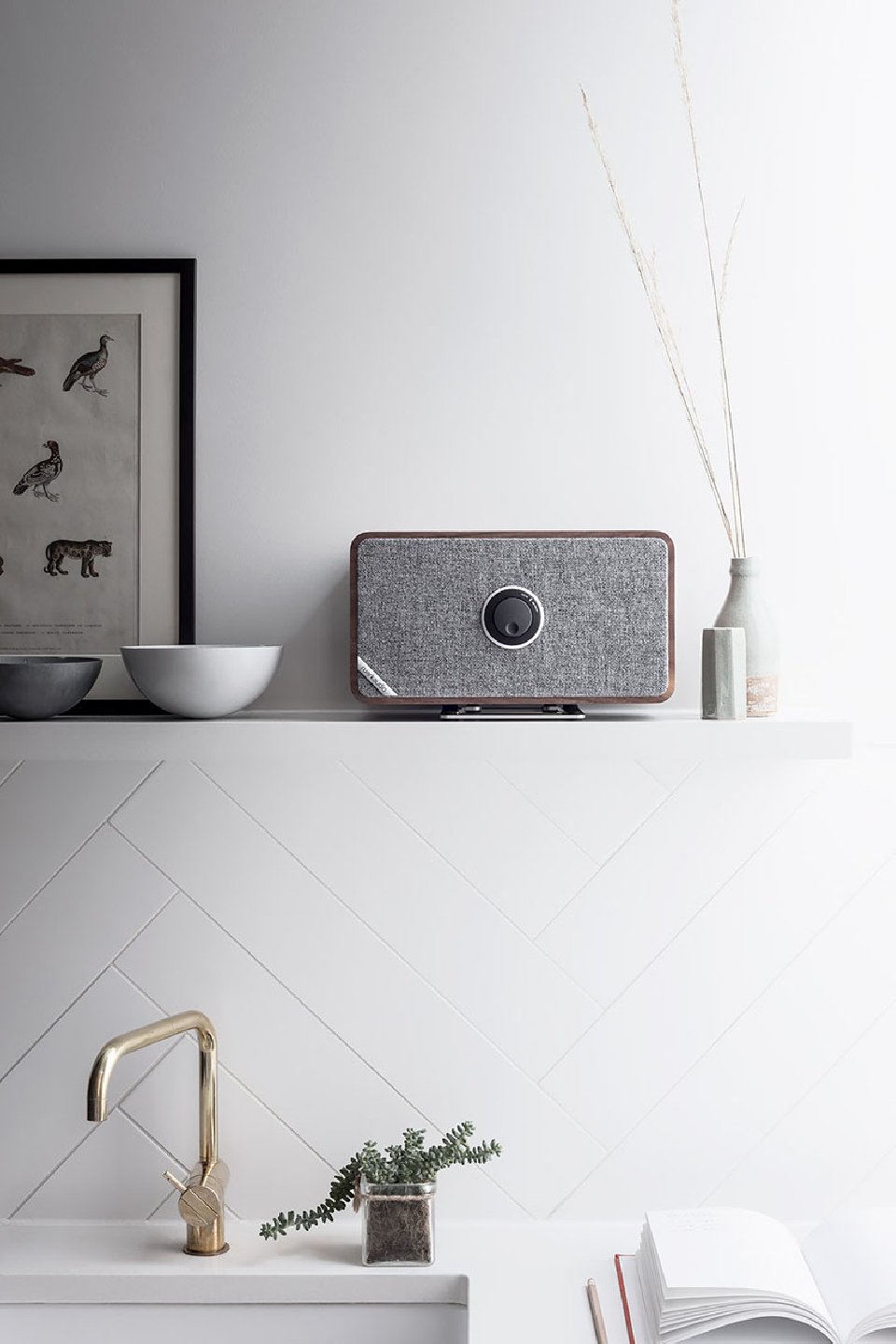Radio on a shelf with a gold faucet and white chevron-patterned tile backsplash in a bright interior setting, featuring minimalist decor.