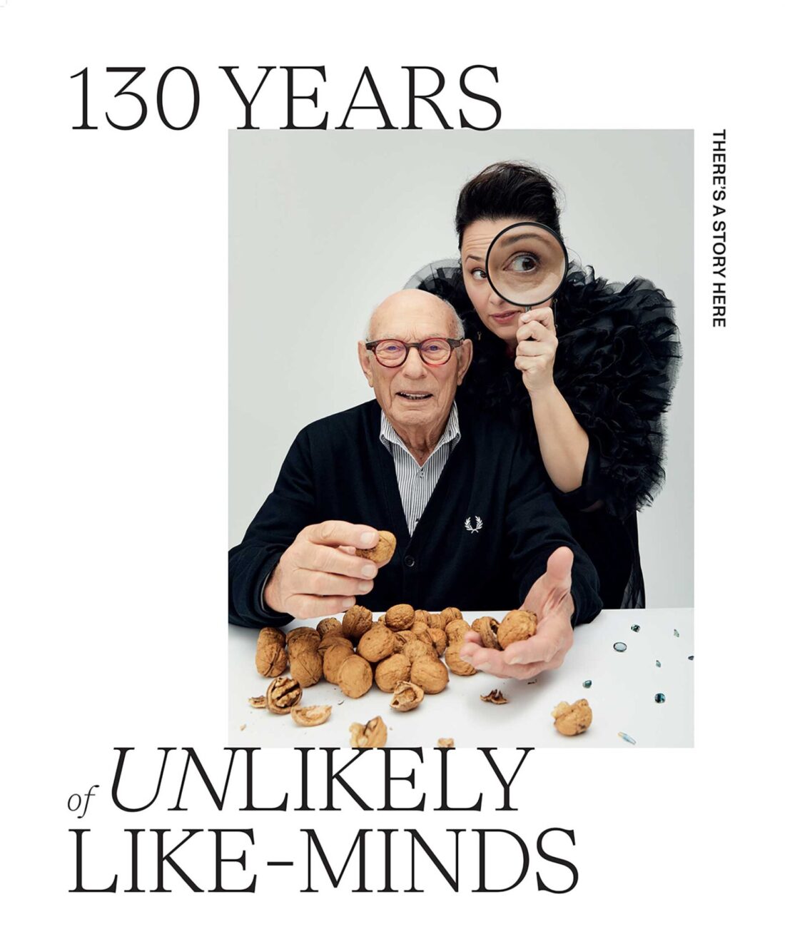 Elderly man and middle-aged woman pose with walnuts, woman peers through a magnifying glass in a studio portrait for a brand advertisement.