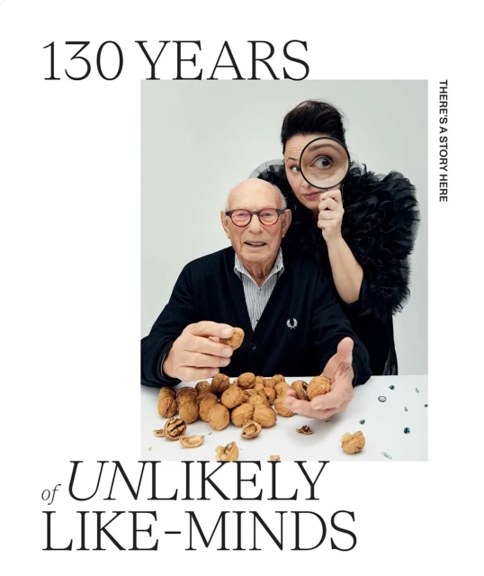 Elderly man and middle-aged woman pose with walnuts, woman peers through a magnifying glass in a studio portrait for a brand advertisement.