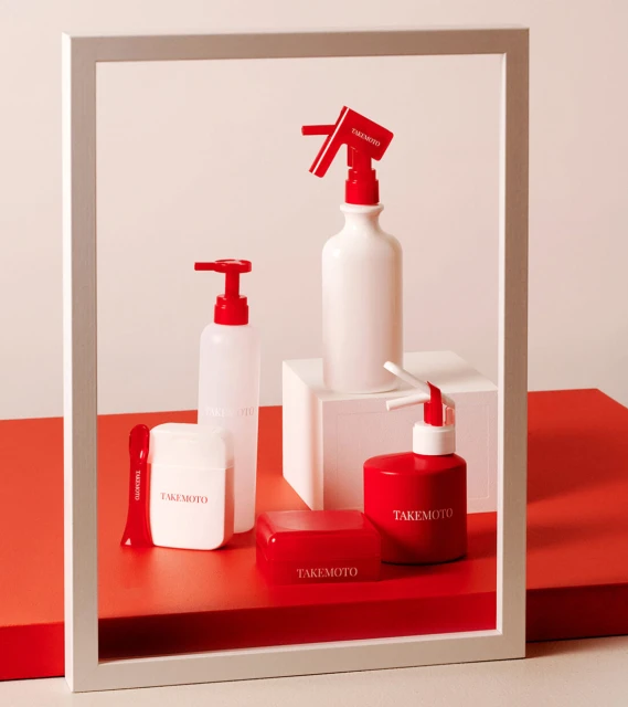 Product shot of TAKEMOTO branded red and white cosmetic bottles and containers, against a white background framed by white border.