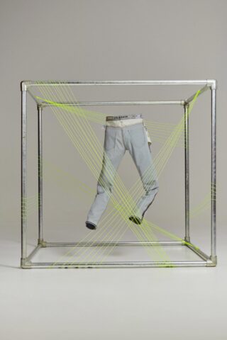 Fashion shot of light wash jeans inside a square metal frame with fluorescent string creating a dynamic display against a neutral background.