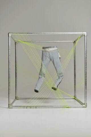 Fashion shot of light wash jeans inside a square metal frame with fluorescent string creating a dynamic display against a neutral background.