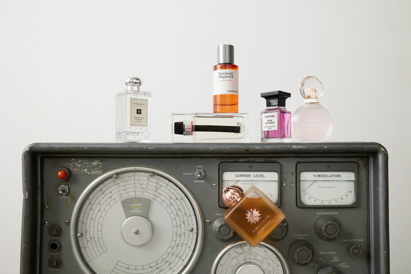 Arrangement of luxury perfume bottles, featuring various brands, sitting atop a vintage radio device against a bright white background.
