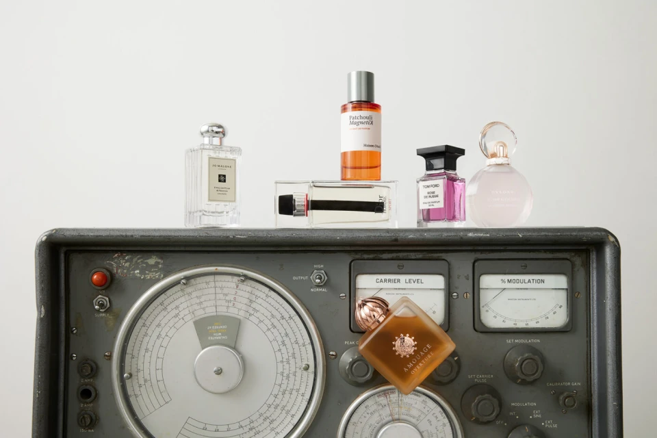 Arrangement of luxury perfume bottles, featuring various brands, sitting atop a vintage radio device against a bright white background.