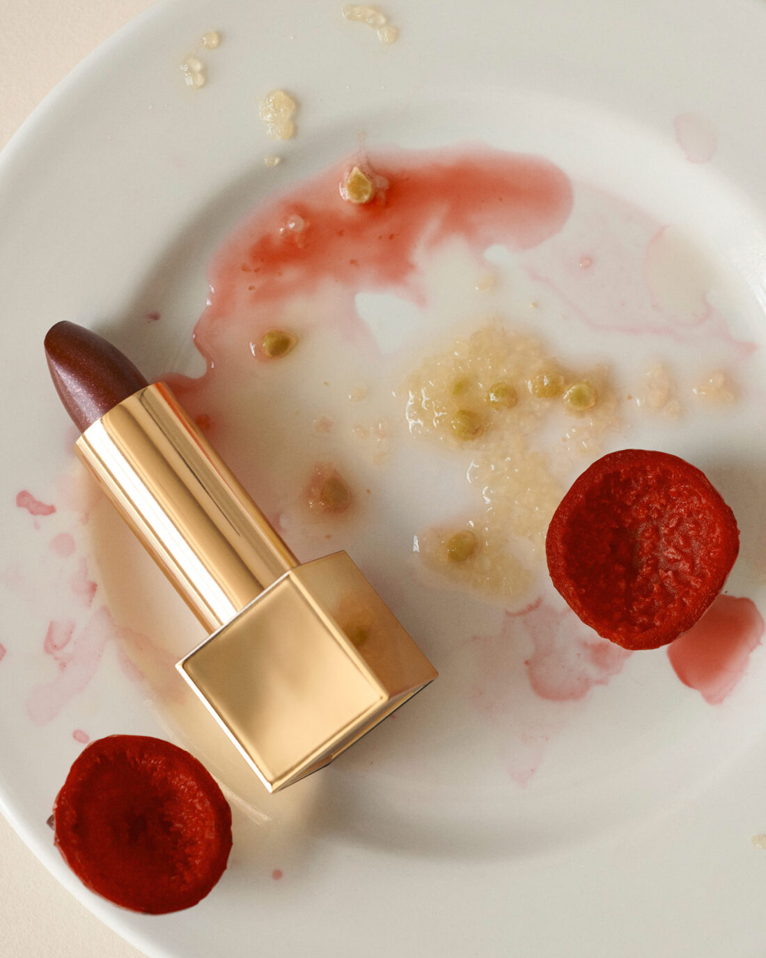 Close-up of lipstick on a white plate with beetroot slices and remnants of food, reflecting beauty in an unconventional setting.