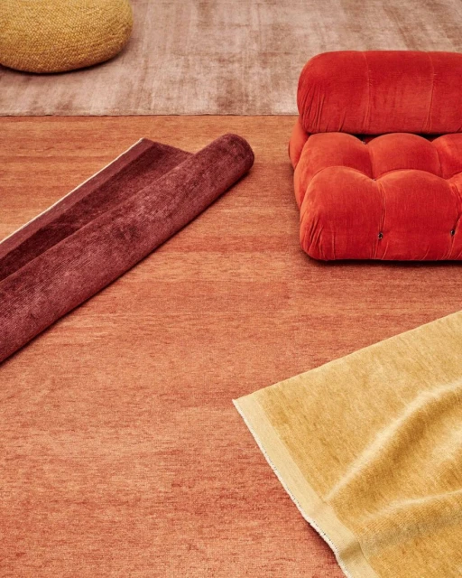Eye-level shot of a layered, monochromatic orange composition featuring carpets, a puffy chair, and a knitted pouf. Warm and inviting.