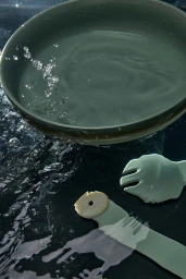 Close-up of a green bowl filled with water and water splashing on a dark surface alongside tableware designed by Natalie Turnbull