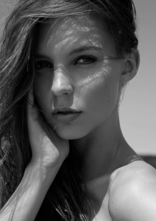 Close-up portrait of a woman in black and white with dappled light across her face and hair styling by Emma Haddock