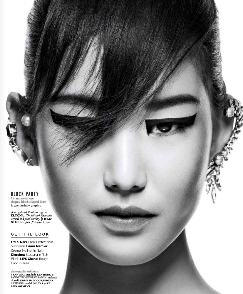 Close-up portrait of a woman with graphic eyeliner, elaborate ear cuffs, and dark hair against a bright backdrop in black and white.