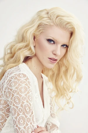Portrait of a blonde woman wearing a white lace top against a seamless white background