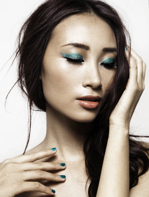 Glamorous close-up of an Asian woman with teal eye makeup and matching nail polish, set against a clean white background.