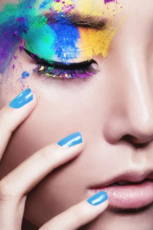 Close-up portrait of a woman with vibrant multi-colored powder eye makeup and bright blue nail polish.