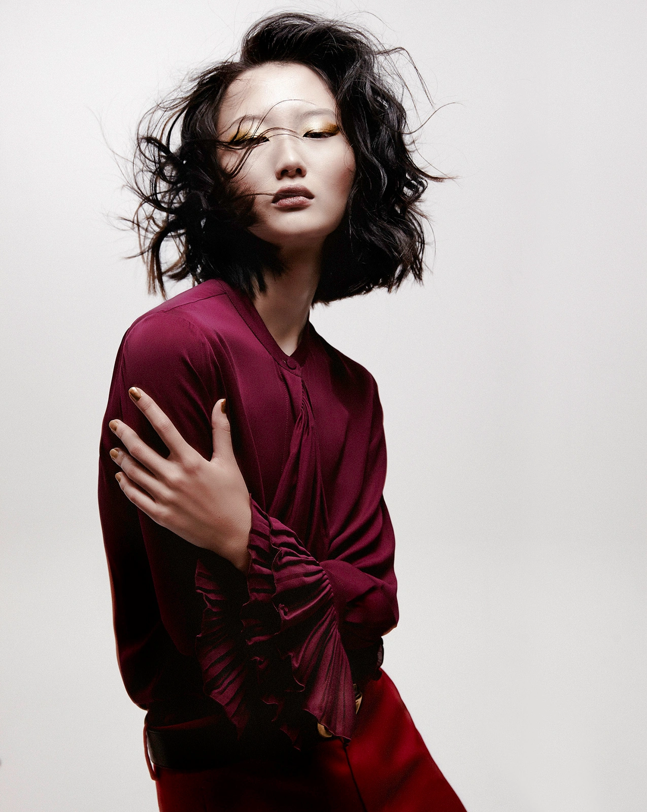 Asian woman with dark wavy hair in a burgundy blouse posing against a plain light background