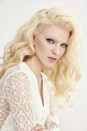 Portrait of a blonde woman wearing a white lace top against a seamless white background