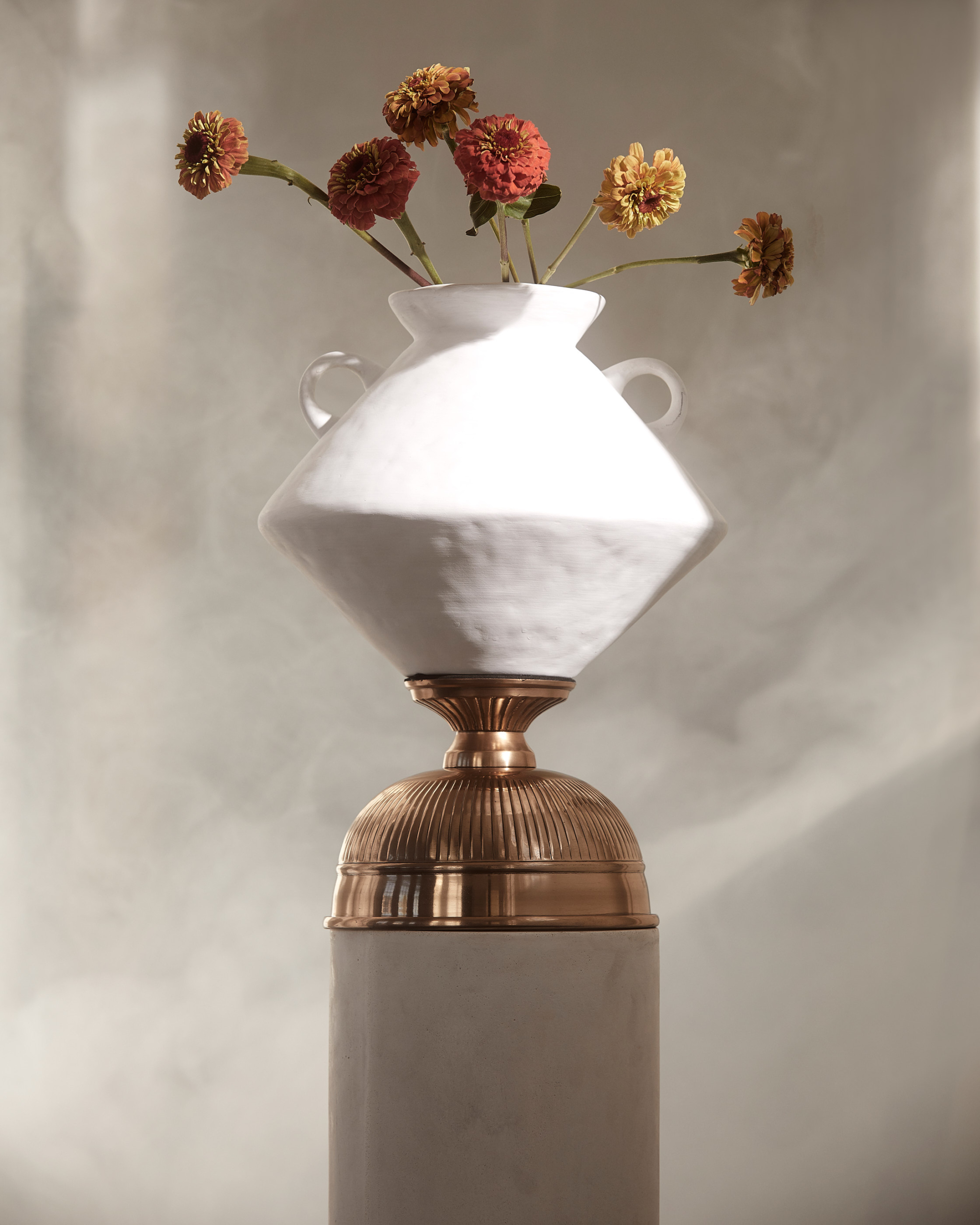 Still life photograph of flowers in a white vase on a pedestal, featuring a soft color palette and elegant composition. 