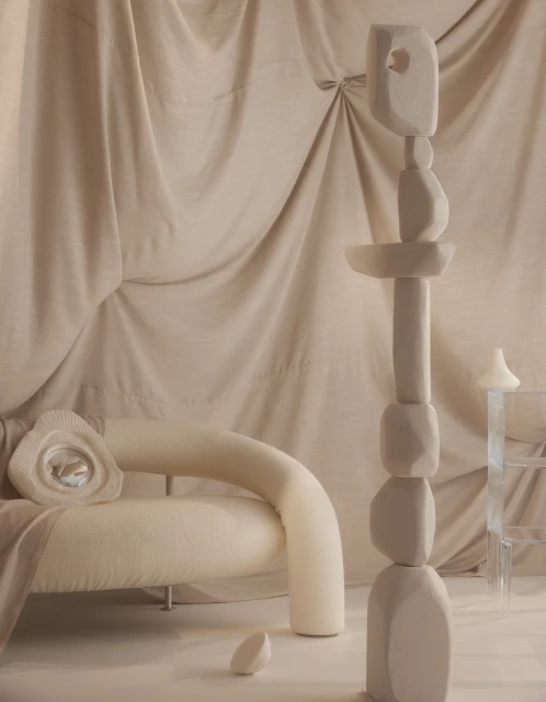 Modern interior with a cream-colored curved sofa, an abstract sculpture, and draped fabric backdrop creates a serene and minimalist space.