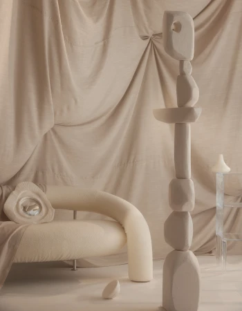 Modern interior with a cream-colored curved sofa, an abstract sculpture, and draped fabric backdrop creates a serene and minimalist space.