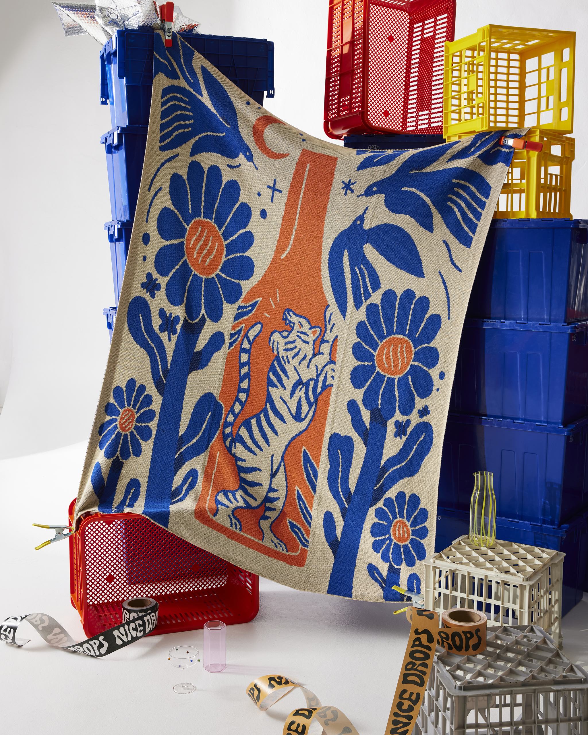 A draped graphic blanket with tigers and flowers in front of stacked blue, red, and yellow crates for product photography in studio.