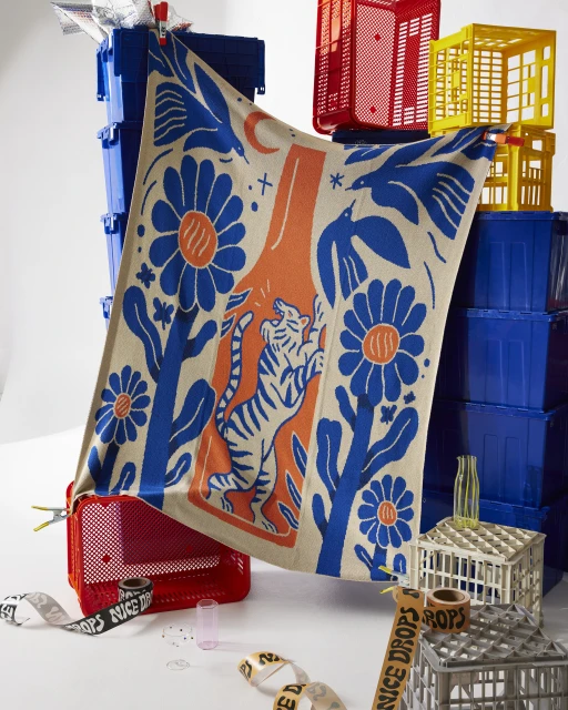 A draped graphic blanket with tigers and flowers in front of stacked blue, red, and yellow crates for product photography in studio.