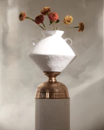 White ceramic vase filled with rust and yellow flowers on a metallic pedestal against a soft textured grey background
