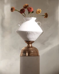 White ceramic vase with handles filled with orange and yellow flowers resting on a metallic pedestal