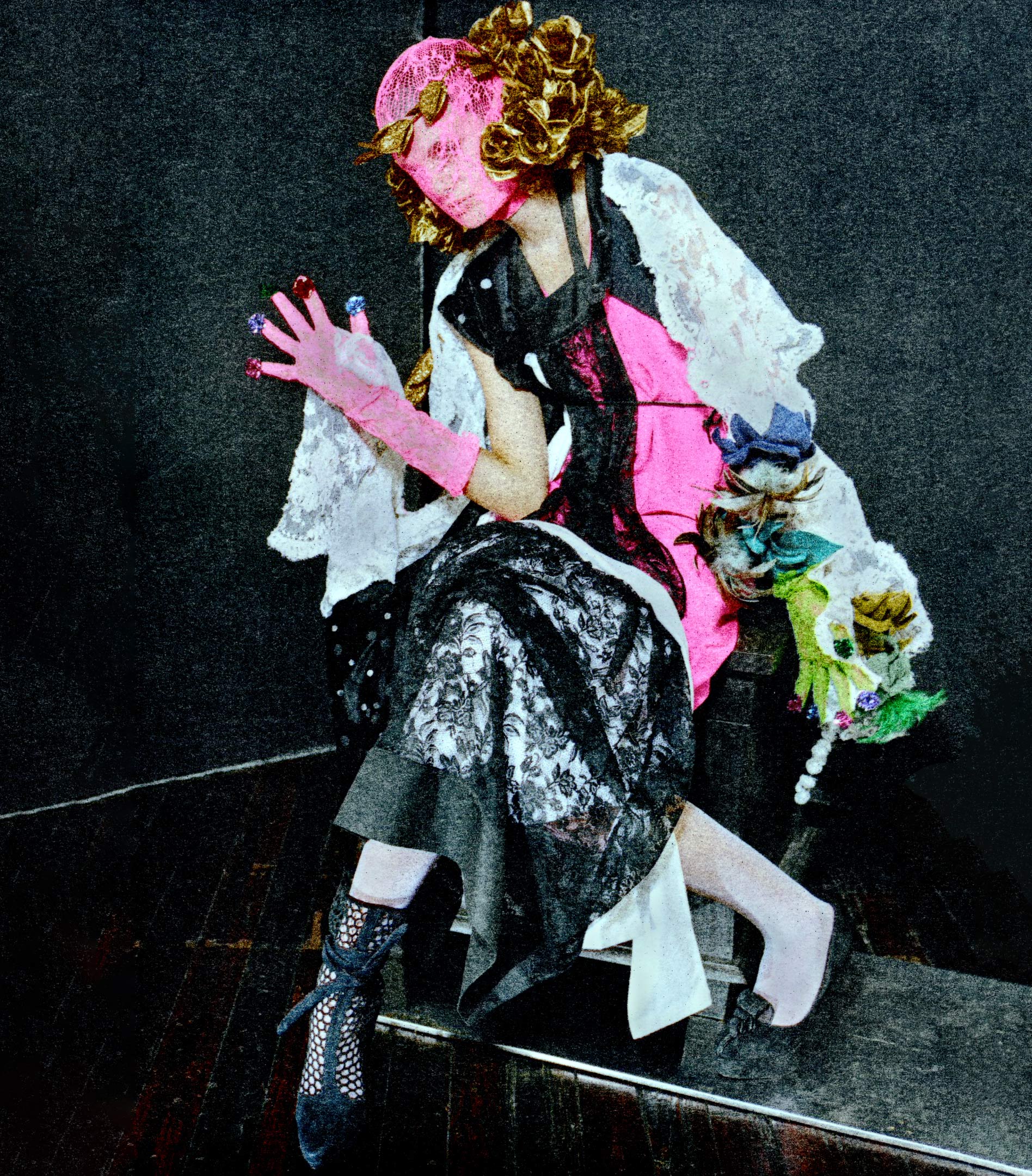 Person in avant-garde fashion, wearing a pink mesh mask, ornate golden hairpiece, and lace dress, posing in a dimly lit indoor setting.