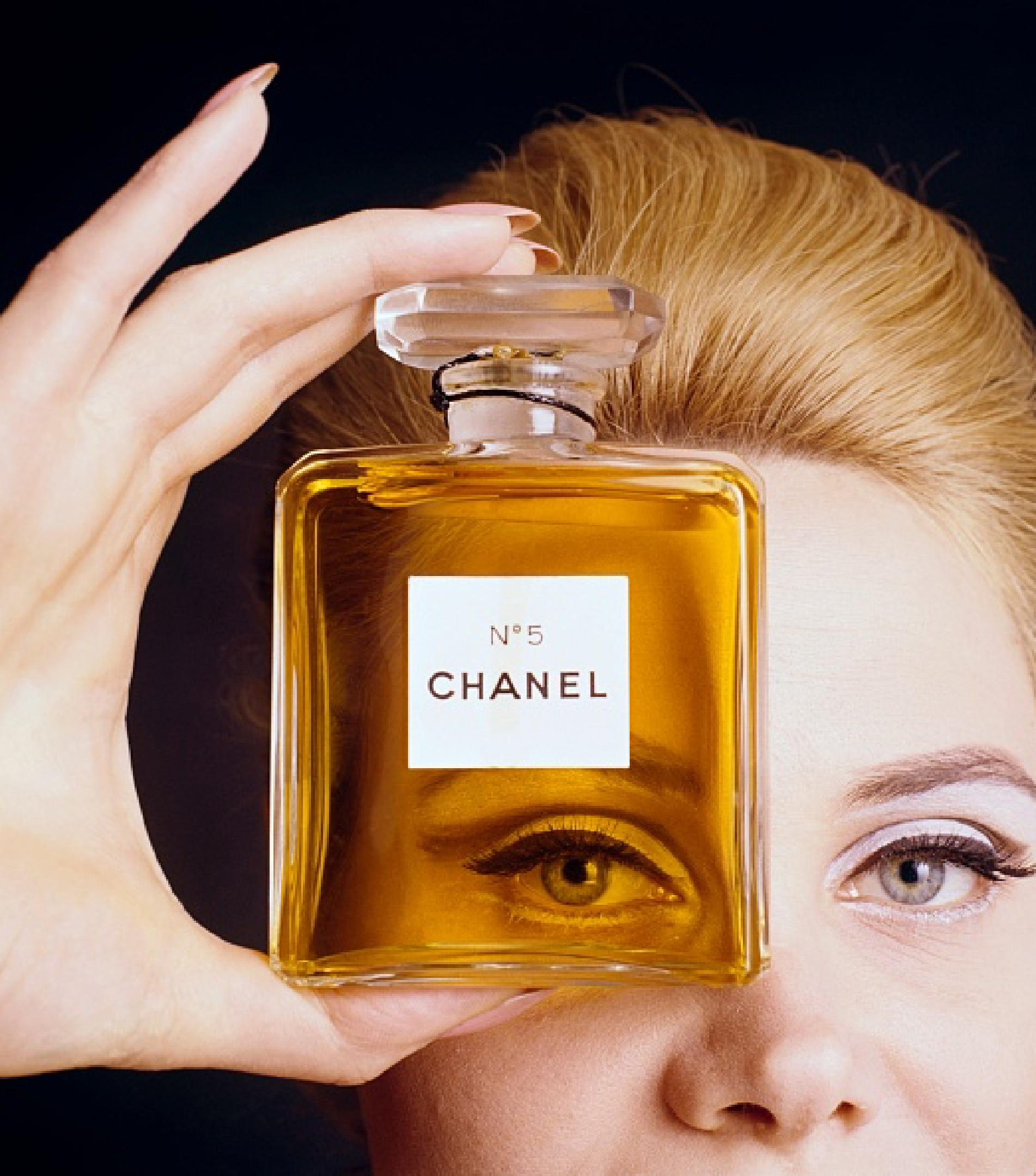 Close-up studio shot of a perfume bottle in front of an adult female's face, featuring visible branding and a classic presentation.
