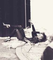 Model lying on the ground surrounded by crumpled plastic wrap wearing black strappy heels and dark patterned tights in Sydney.
