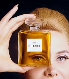 Close-up of a woman holding a rectangular perfume bottle with Chanel No 5 label partially obscuring her face.