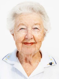 Close-up portrait of an elderly woman smiling gently against a bright white background, wearing a white collared shirt.