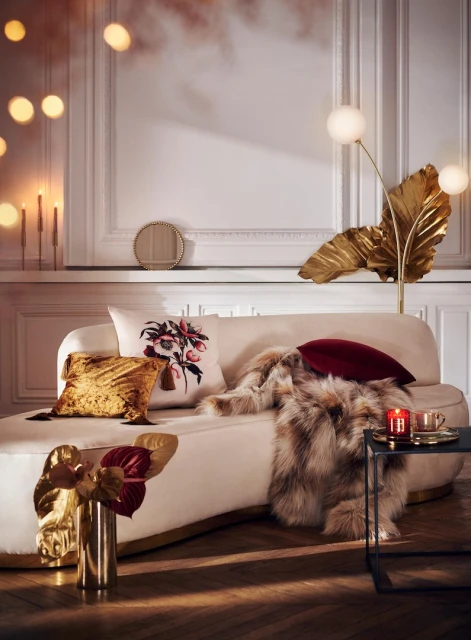 Living room interior featuring a cream chaise lounge with gold accents, decorative pillows, gold leaf decor, and accent table.
