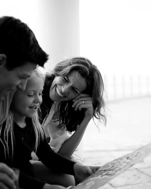 Black and white photo of a family of three—father, mother, and daughter—looking at something together and smiling in an indoor environment.