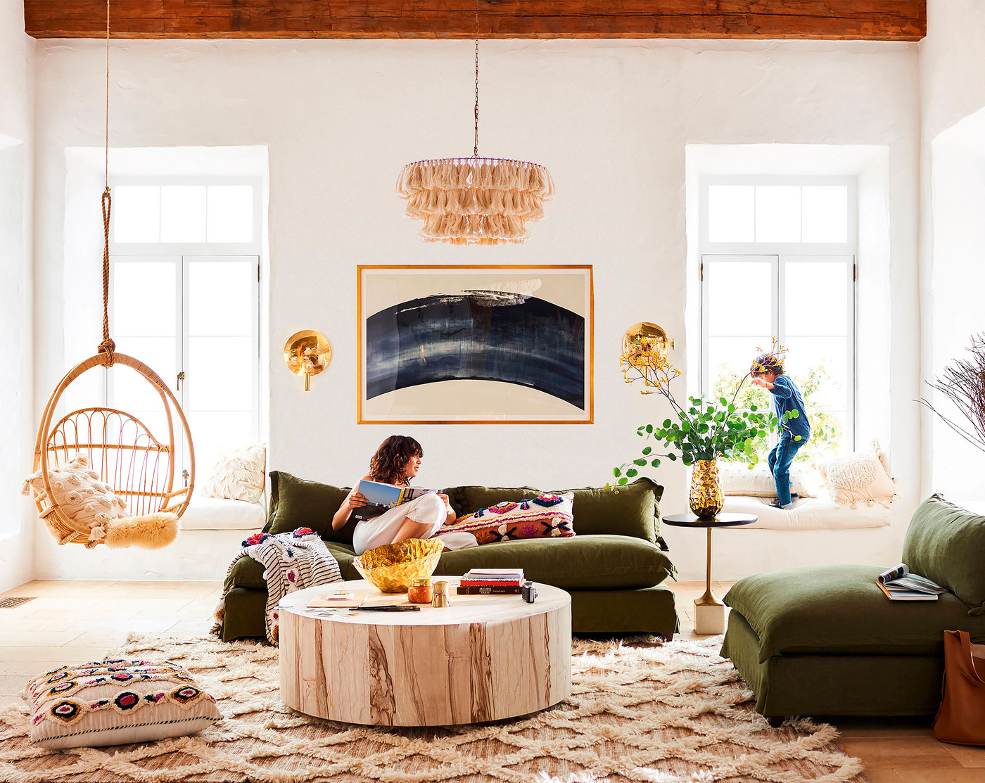 A woman reads a book on a sofa in a living room with a child by the window, swing chair, modern art, and natural light.