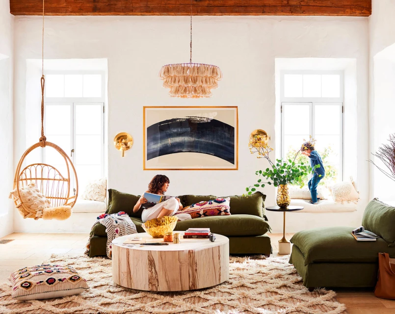 A woman reads a book on a sofa in a living room with a child by the window, swing chair, modern art, and natural light.