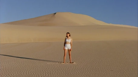 Woman in white underwear standing alone on a vast desert sand dune under a clear blue sky