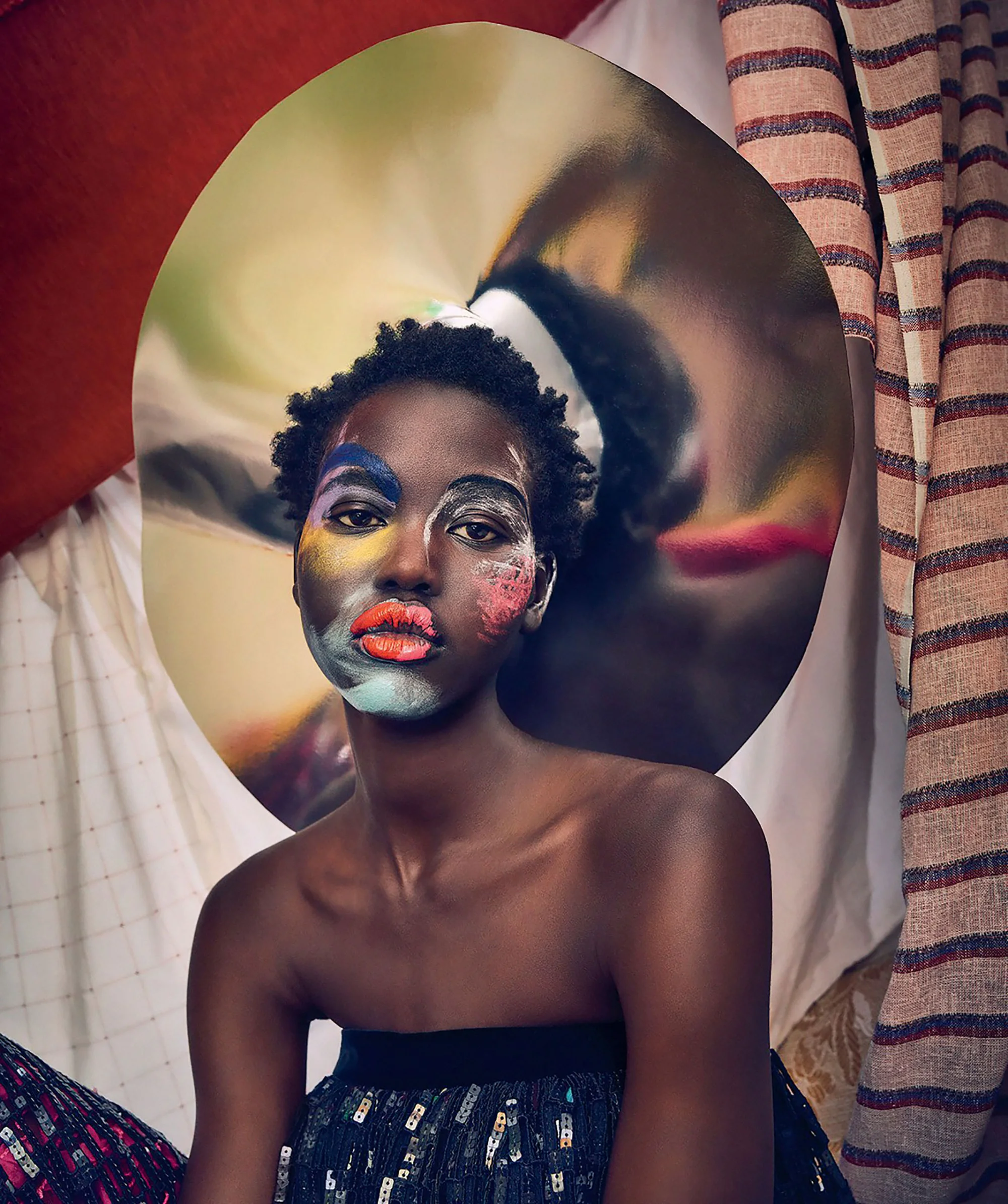 Close-up portrait of a Black woman with colorful face paint, posing in an indoor setting with striped drapery in the background.