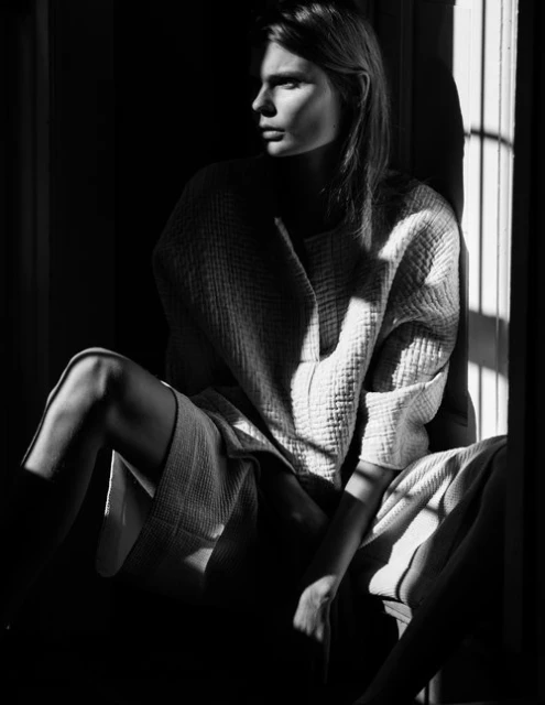 Monochrome portrait of a woman with medium-length hair, wearing a light textured dress, seated with light and shadow play.