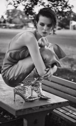 Model with dark short hair wearing a silk slip dress and shiny metallic boots crouching on a park bench