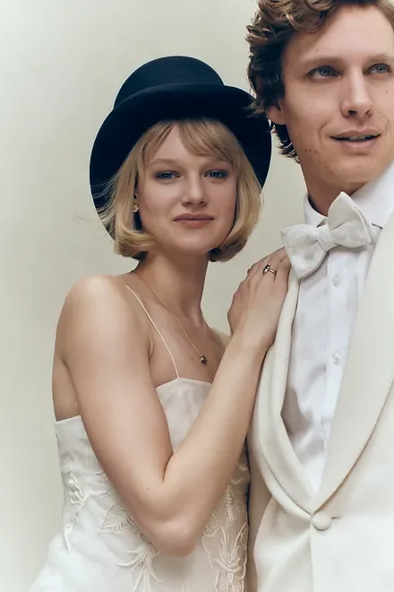 Woman in a black bowler hat and cream slip dress standing beside a man in a white tuxedo jacket and bow tie