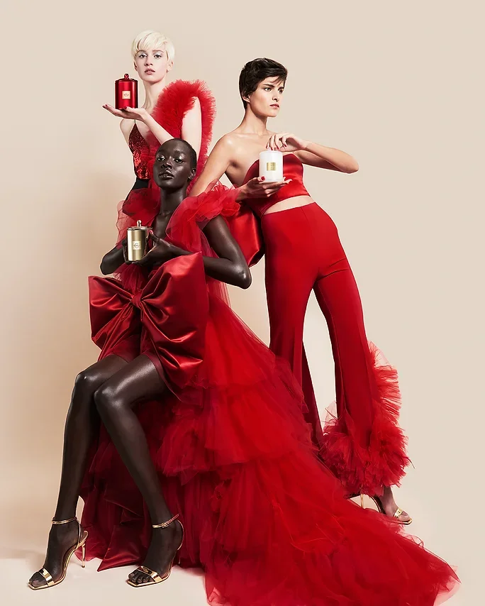 Three models wearing red attire holding perfume bottles against a neutral backdrop, produced by Laura Midalia.