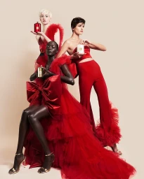 Three models wearing red attire holding perfume bottles against a neutral backdrop, produced by Laura Midalia.