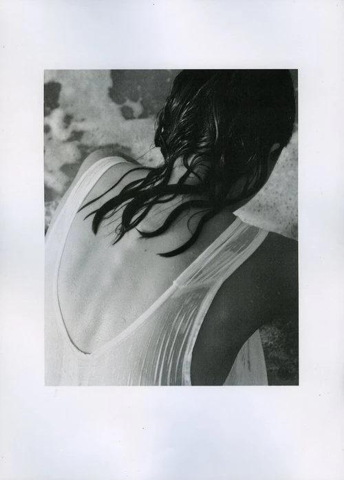 Black and white portrait of a woman with wet hair wearing a wet white tank top against water background.