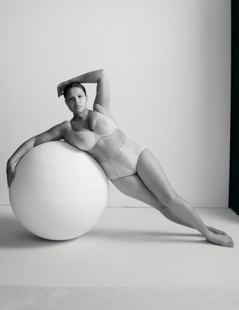 Portrait of a woman in lingerie leaning against a large white ball in a photo studio with a minimalist aesthetic and monochrome color palette.